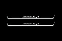 Two long door sill plates with Mach-E 4X lettering and edges illuminated in white, straight-on view on a dark background.