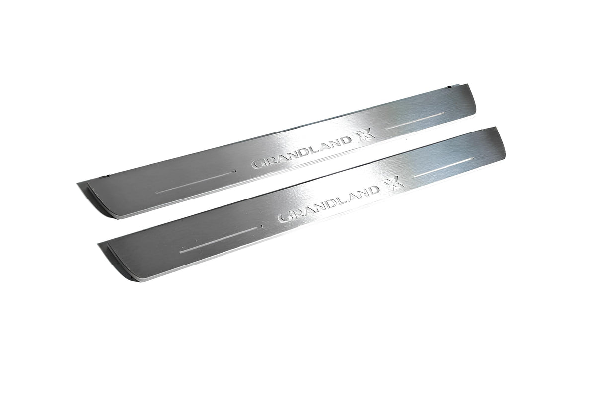 Two long silver-finished door sill plates with Grandland X lettering on a light background, angled view.