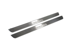 Two long silver-finished door sill plates with Brabus lettering on a light background, angled view.