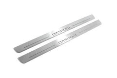 Two long silver-finished door sill plates with Qashqai lettering on a light background, angled view.
