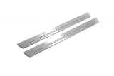 Two long silver-finished door sill plates with M Performance lettering on a light background, angled view.