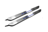 Two narrow silver door sill inserts with blue M Performance lettering and attached wires, angled view on a white background.