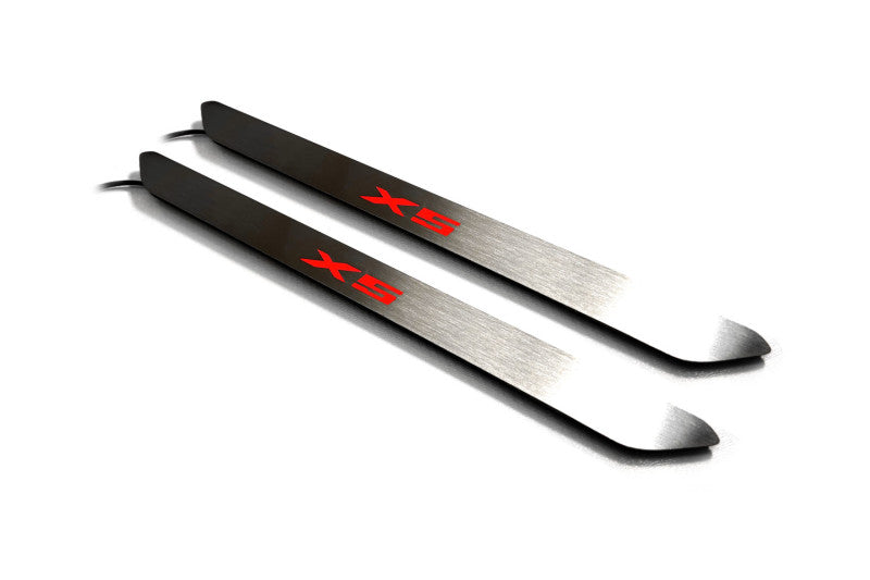 Two narrow silver door sill inserts with red X5 lettering and attached wires, angled view on a white background.