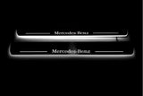 Two long door sill plates with Mercedes-Benz lettering and edges illuminated in white, straight-on view on a dark background.