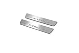 Two short silver-finished door sill plates with X-Trail lettering on a light background, angled view.
