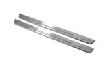 Two long silver-finished door sill plates with M Performance lettering on a light background, angled view.