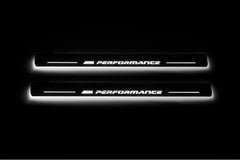 Two long door sill plates with M Performance lettering and edges illuminated in white, straight-on view on a dark background.