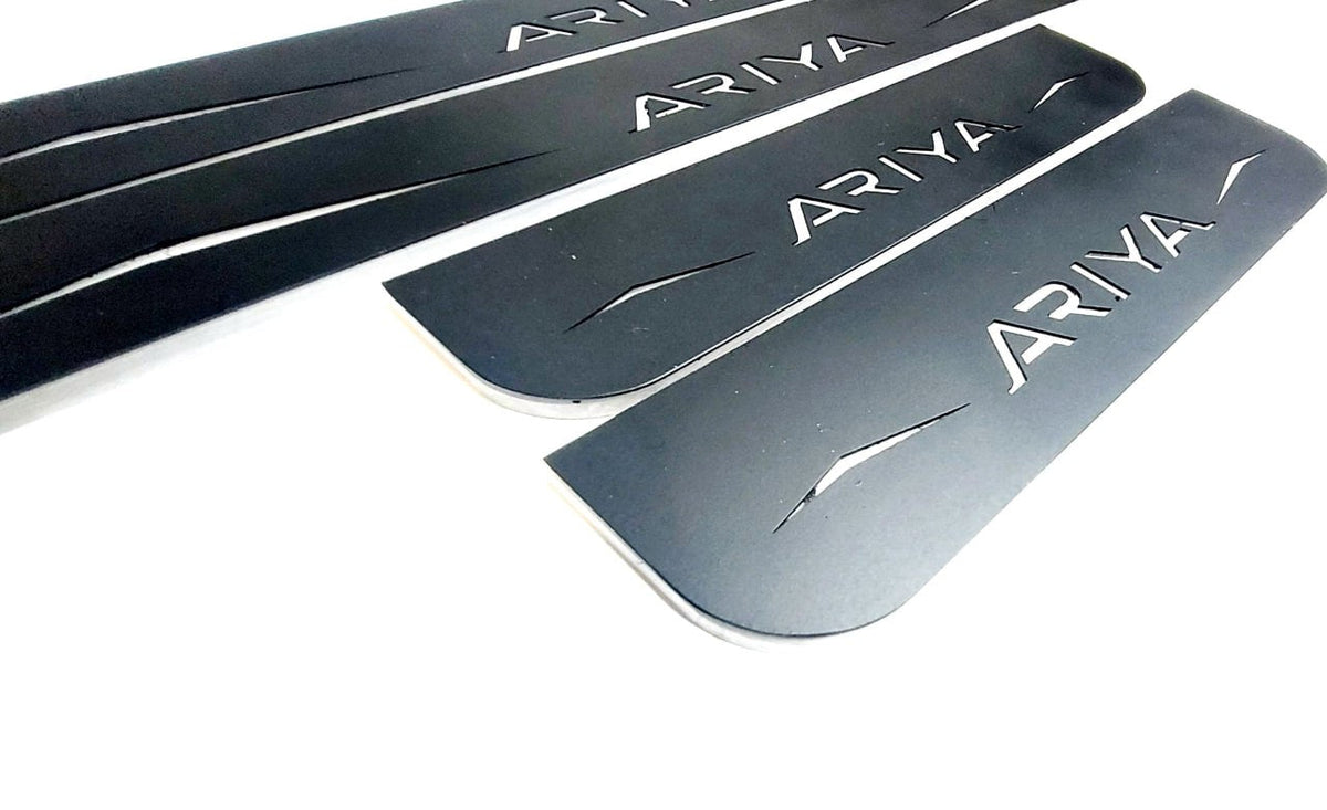 Close-up of four reflective dark-finished Ariya door sill plates and their angular graphics.