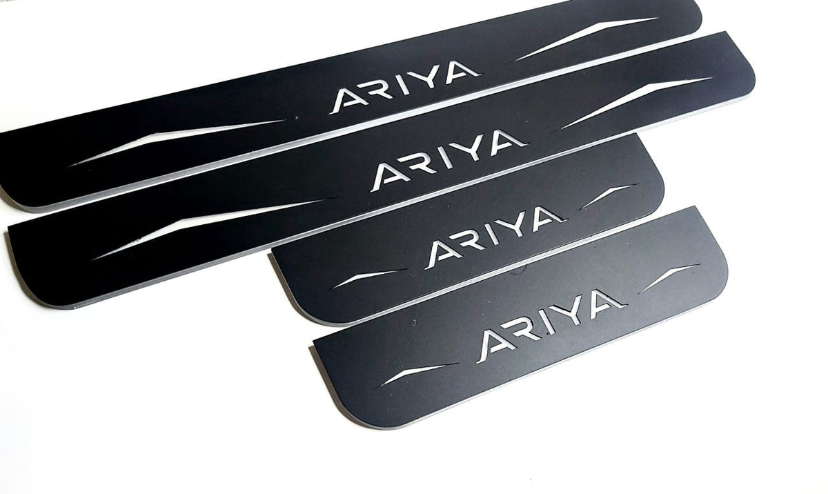 Four reflective dark-finished Ariya door sill plates with angular graphics on a white background, angled view.