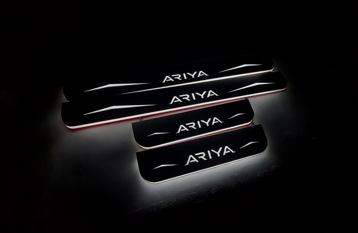 Four dark door sill plates with Ariya lettering, angular graphics and illuminated edges on a black background, angled view.