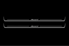 Two long door sill plates with Accord lettering and edges illuminated in white, straight-on view on a dark background.