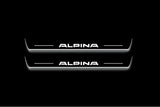 Two long door sill plates with Alpina lettering and edges illuminated in white, straight-on view on a dark background.