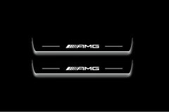 Two long door sill plates with AMG lettering and edges illuminated in white, straight-on view on a dark background.