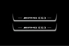 Two long door sill plates with AMG E63 lettering and edges illuminated in white, straight-on view on a dark background.