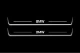 Two long door sill plates with BMW lettering and edges illuminated in white, straight-on view on a dark background.