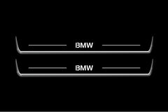 Two long door sill plates with BMW lettering and edges illuminated in white, straight-on view on a dark background.