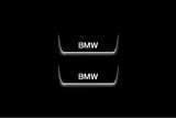 Two short door sill plates with BMW lettering and edges illuminated in white, straight-on view on a dark background.