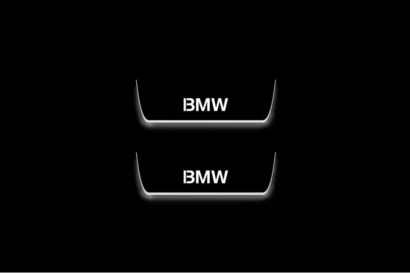 Two short door sill plates with BMW lettering and edges illuminated in white, straight-on view on a dark background.