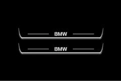 Two long door sill plates with BMW lettering and edges illuminated in white, straight-on view on a dark background.