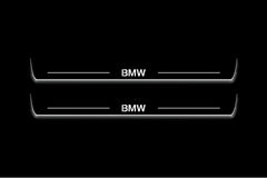 Two long door sill plates with BMW lettering and edges illuminated in white, straight-on view on a dark background.