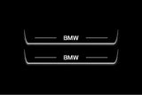Two long door sill plates with BMW lettering and edges illuminated in white, straight-on view on a dark background.