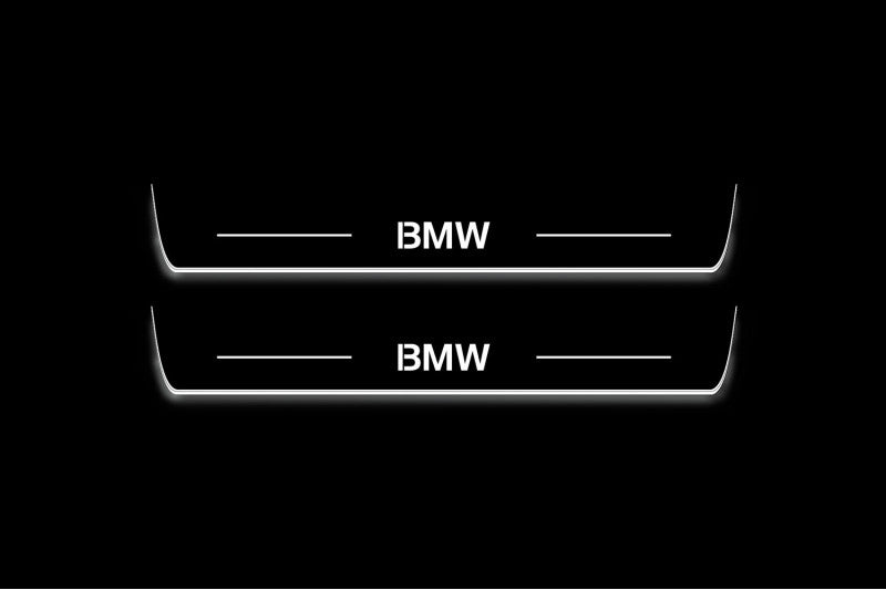 Two long door sill plates with BMW lettering and edges illuminated in white, straight-on view on a dark background.