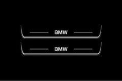 Two long door sill plates with BMW lettering and edges illuminated in white, straight-on view on a dark background.