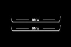 Two long door sill plates with BMW lettering and edges illuminated in white, straight-on view on a dark background.