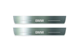 Two long silver-finished door sill plates with BMW lettering on a light background, straight-on view.