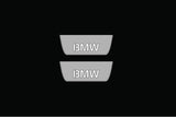 Catalog illustration of two short gray door sill plates with BMW lettering on a black background.