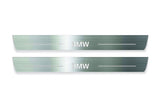 Two long silver-finished door sill plates with BMW lettering on a light background, straight-on view.