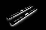 Two exact angled BMW M-logo Stainless front sill plates, dark Night view, three separated white M stripes, paired white lines and real white side glow.