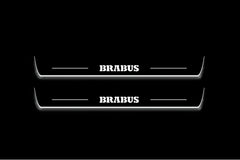 Two long door sill plates with Brabus lettering and edges illuminated in white, straight-on view on a dark background.