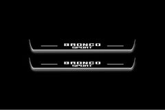 Two long door sill plates with Bronco Sport lettering and edges illuminated in white, straight-on view on a dark background.
