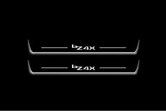 Two long door sill plates with bZ4X lettering and edges illuminated in white, straight-on view on a dark background.