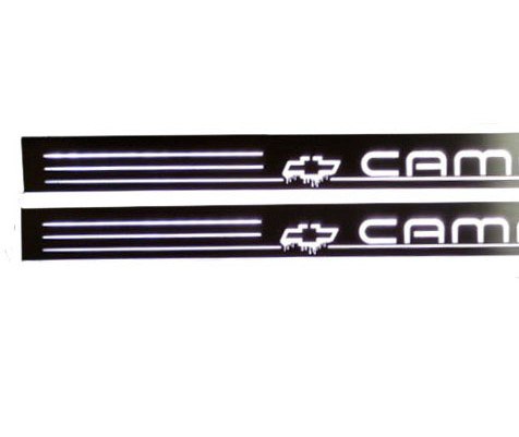 Close-up of white Camaro lettering, Chevrolet bowtie emblems and horizontal stripes on dark reflective door sill plates.