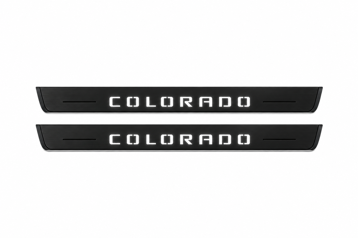 Catalogue illustration of two black Matte PRO front door sill plates with illuminated geometric COLORADO lettering on the upper surface. Decorative lines and edges are unlit; rear plates for FRONT+REAR are not pictured. Dimensions are selected for the Chevrolet Colorado II during manufacture.
