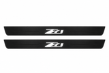 Catalogue illustration of two black Matte PRO front door sill plates with illuminated Z71 lettering on the upper surface. Decorative lines and edges are unlit; rear plates for FRONT+REAR are not pictured. Dimensions are selected for the Chevrolet Colorado II during manufacture.