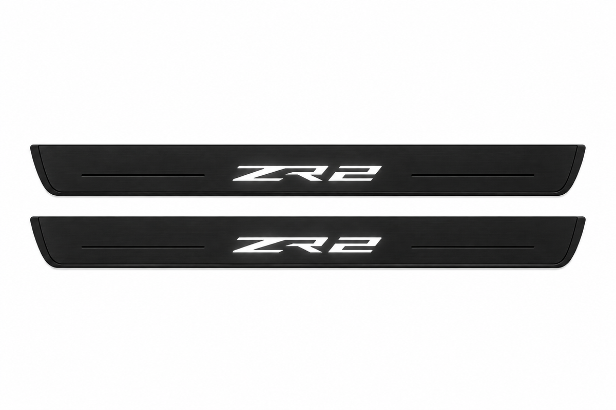 Catalogue illustration of two black Matte PRO front door sill plates with illuminated ZR2 lettering on the upper surface. Decorative lines and edges are unlit; rear plates for FRONT+REAR are not pictured. Dimensions are selected for the Chevrolet Colorado II during manufacture.