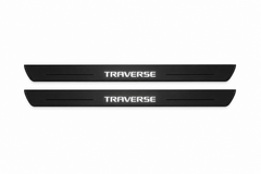 Catalogue illustration of two black Matte PRO front door sill plates with illuminated geometric TRAVERSE lettering on the upper surface. Thin decorative lines and edges are unlit; rear plates for FRONT+REAR are not pictured. Dimensions are selected for the Chevrolet Traverse C1XX during manufacture.