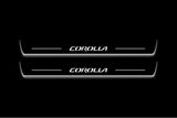 Two long door sill plates with Corolla lettering and edges illuminated in white, straight-on view on a dark background.