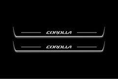 Two long door sill plates with Corolla lettering and edges illuminated in white, straight-on view on a dark background.