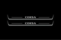 Two long door sill plates with Corsa lettering and edges illuminated in white, straight-on view on a dark background.