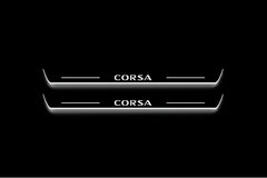 Two long door sill plates with Corsa lettering and edges illuminated in white, straight-on view on a dark background.