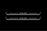 Two long door sill plates with CX-30 lettering and edges illuminated in white, straight-on view on a dark background.