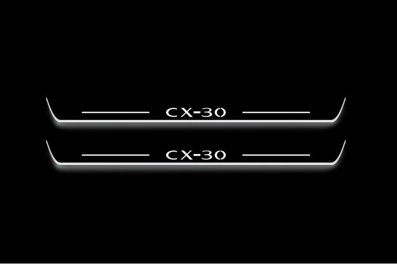 Two long door sill plates with CX-30 lettering and edges illuminated in white, straight-on view on a dark background.