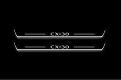 Two long door sill plates with CX-30 lettering and edges illuminated in white, straight-on view on a dark background.