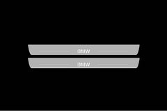 Catalog illustration of two long gray door sill plates with white BMW lettering and horizontal lines on a black background.