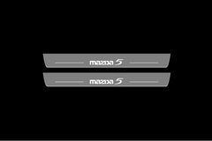 Catalog illustration of two gray door sill plates with Mazda5 lettering on a black background.