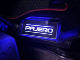 Short rectangular Pajero plate illuminated beside a vehicle floor mat; installation example.